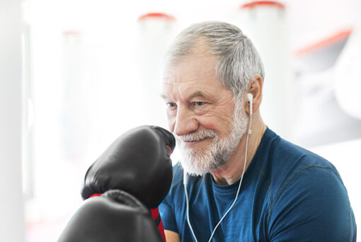 Fit senior man with earphones and boxing gloves in gym